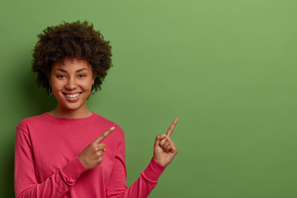 緑色の背景の前に立って笑顔を浮かべている若い黒人女性の写真